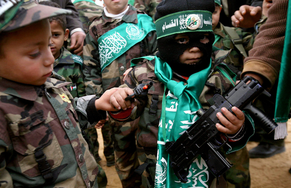 Un niño palestino, vestido como un militante de Hamas, sostiene dos armas de juguete.